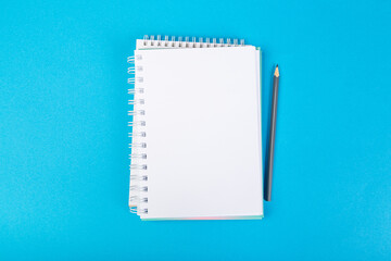 school notebooks on a blue background, spiral notepad with a blank page and a pencil on the table top view