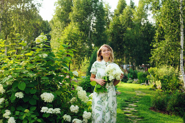 beautiful young woman gardener posing with hydrangea flowers in summer cottage garden