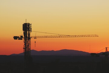 Fototapeta premium Grúa torre de construcción al atardecer. Silueta de la grúa sobre un bonito fondo anaranjado con los últimos rayos de sol en Madrid, España.
