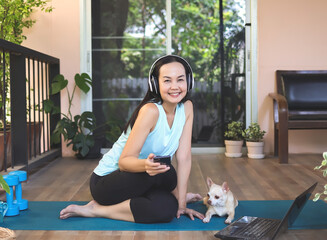 sitting  on yoga mat in balcony  with computer laptop dumbbell and Chihuahua dog., smiling and looking at camera. Yoga training online