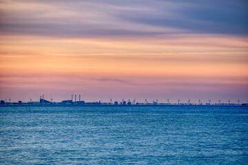 Fototapeta premium Copenhagen skyline at sunset with turbines rotating away in the Danish wind farm. Baltic Sea wind power plant with the city 's industrial skyline raises concerns about pollution and sustainable energy