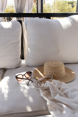 Women's fashion accessories. Stylish female sunglasses, straw hat, shopper bag on white lounge couch with pillows