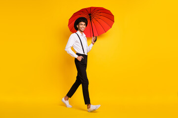 Full length photo portrait of african american man walking with red umbrella isolated on vivid yellow colored background