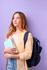 Caucasian girl teen student in casual wear with backpack and books isolated on purple background studio portrait