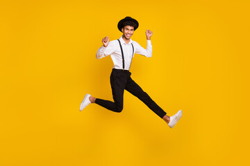 Fototapeta na wymiar Photo of funky crazy guy jump raise fists wear headwear shirt suspenders sneakers isolated yellow color background