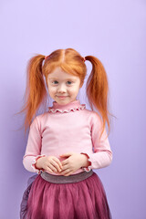 Shy diligent redhead kid girl with two pony tails posing at camera, smiling
