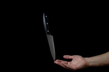 Knife on the hand on a dark background. The knife balances on a finger against a black background....