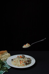 Pilaf on a black background. A spoonful of pilaf over a plate. Creative food photography on dark background