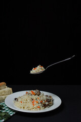 Pilaf on a black background. A spoonful of pilaf over a plate. Creative food photography on dark background