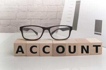 The word ACCOUNT ON WOODEN cubes on a light office background with glasses and papers, business concept