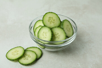Bowl with cucumber slices on white textured background