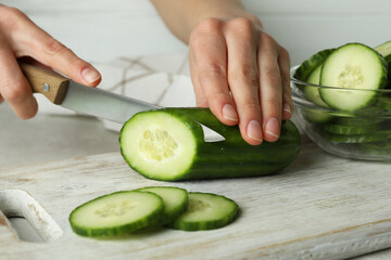 Woman cuts a cucumber on wooden board