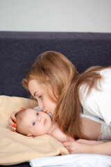 Closeup Portrait of Young Careful Caucasian Girl Embracing and Kissing Her Newborn Brother Lying on Bed.