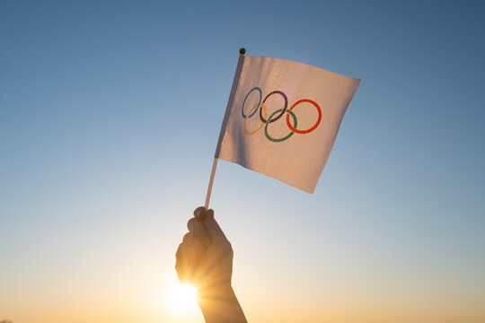 The Olympic flag, small in hand, flutters against the backdrop of blue sky and setting sun. Concept for Winter and Summer Olympic Games, 2021, 2022.