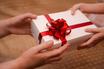 Closeup Image of Mature Woman Wrinkled Hands Holding and Offering White Wrapped Gift Box to the Hands of Young Girl.