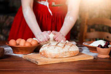 Hands of Female in Rural Decorated Dress Kneading Dough For Bread Baking with Lots of Countryside Products.Placed on Table.