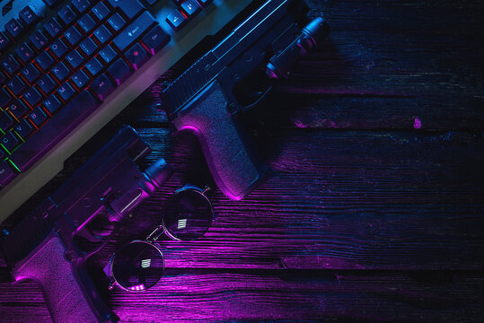 Cyberpunk concept flat lay background with copy space. Guns and computer keyboard on the table background in the neon lights.