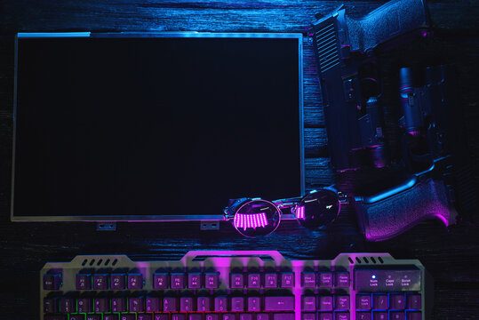 Cyberpunk concept flat lay background with copy space. Blank computer monitor display wit copy space, guns and computer keyboard on the table background in the neon lights.