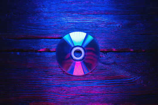 Cd disk in the neon lights on the black flat lay table background. - Powered by Adobe