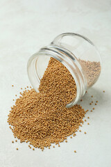 Glass jar with mustard seeds on white textured background
