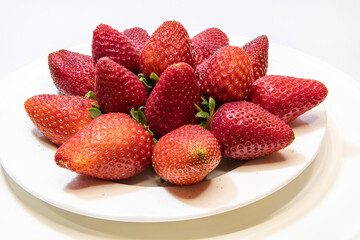 Pile of selected red garden strawberry on white kitchen saucer