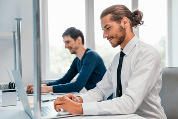side view. smiling business man working on a laptop.