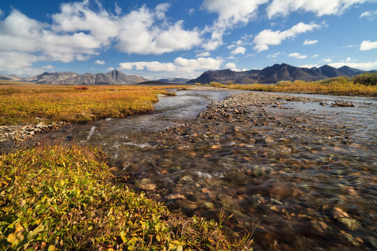 Beautiful autumn Arctic landscape. A small river in the tundra. Mountains in the distance. Travel and hiking in the wilderness in the Far North in the Polar Region. Nature of Chukotka. Far East Russia