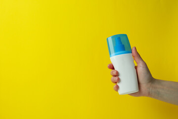 Female hand hold sunscreen on yellow background