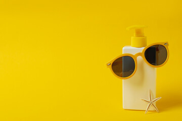 Bottle of sunscreen with sunglasses and starfish on yellow background