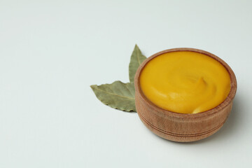 Naklejka na ściany i meble Wooden bowl with mustard and leaves on white background