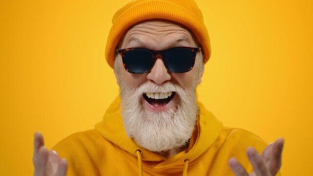 Old man having fun indoor. Joyful guy gesticulating on yellow studio background.