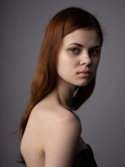 Portrait of a romantic red-haired woman with bare shoulders on a gray background