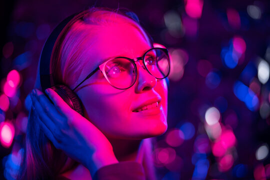 Mysterious hipster teenager in glasses listening to music with headphones. Portrait of millennial pretty girl with short hairstyle with neon light. Dyed blue and pink hair.