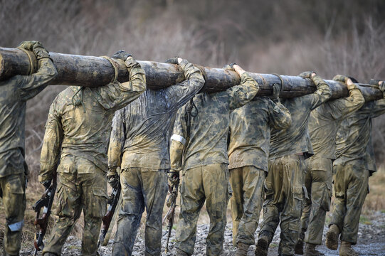 Special forces military training carrying a big log. Photograph detail with military equipment and assault rifle.