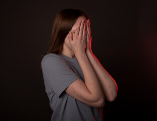 Young woman hiding and covering her face with hands, palms in fear or frustration