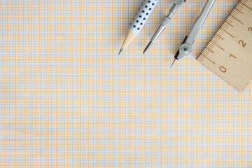 Wooden ruler, compasses and pencil lie on graph paper