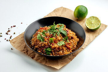 Appetizing Asian street food rice wok with chicken, hot peppers, vegetables, cilantro, served in a black plate on a white plate. Popular Pan-Asian cuisine