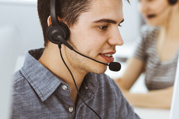 Casual dressed young man using headset and computer while talking with customers online. Group of operators at work. Call center
