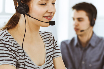 Casual dressed young woman using headset and computer while talking with customers online. Group of operators at work. Call center, business concept