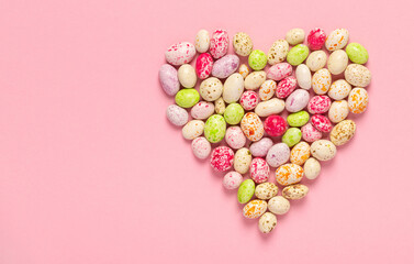 Glazed candies in the shape of a heart on a pink background with copy space.