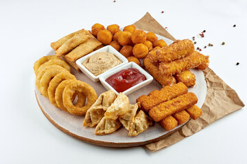 Appetizing beer snack - a set of deep-fried snacks, mozzarella, onion rings, fish sticks, potato croquettes with sauce and on a wooden board. White background.