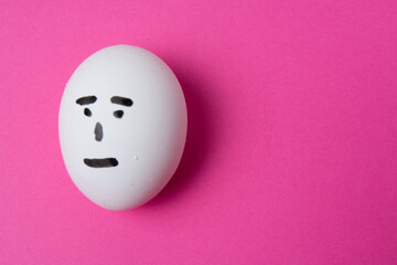 Egg with an indifferent face, on a pink background with copy space.