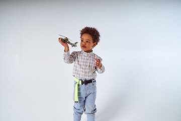 Little African-American boy sits with toy helicopter on white background