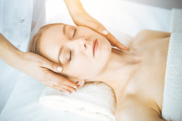 Happy woman enjoying facial massage with closed eyes in spa salon. Relaxing treatment in medicine and Beauty concept