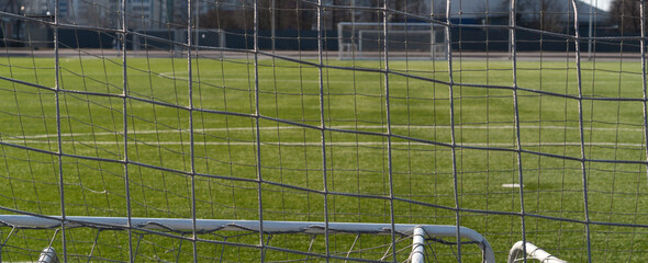 Fototapeta premium View through the net of a soccer goal, football gate. Green synthetic grass sports field with white line shot. Sports background.