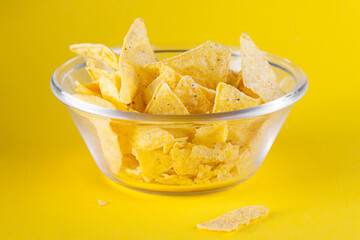 Nachos chips in glass bowl on yellow background