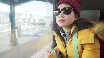 lifestyle portrait of young happy and beautiful Asian Korean woman in yellow jacket and hat looking through train window traveling during winter holiday