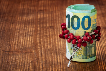 Catholic  rosary with beads and roll of Euro currency on a dark brown wooden table