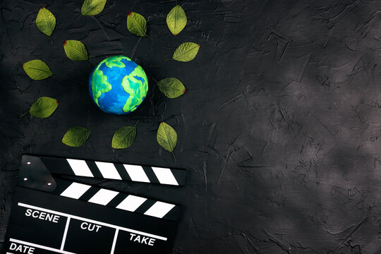 Movie clapper board and globe surrounded by leaves on black background.