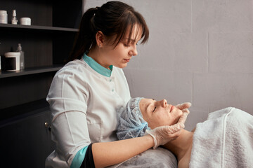 A young female cosmetologist does a facial massage in gloves. Professional beauty salon.